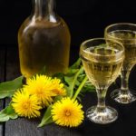 Cooled-homemade-dandelion-wine-in-old-wineglasses-bottle-and-wreath-from-dandelions-on-a-dark-background