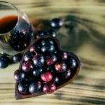 Red-wine-in-crystal-stemless-glass-with-wooden-heart-shaped-bowl-filled-with-Muscadine-grapes-on-burned-wooden-background