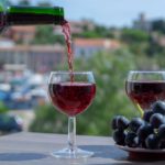 Waiter-pouring-red-wine-on-outdoor-cafe-terrace-in-sunny-summer-day-in-France