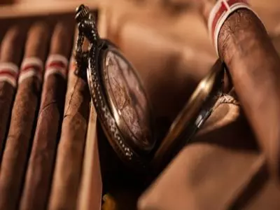 cigars  laying together with a timepiece in the middle