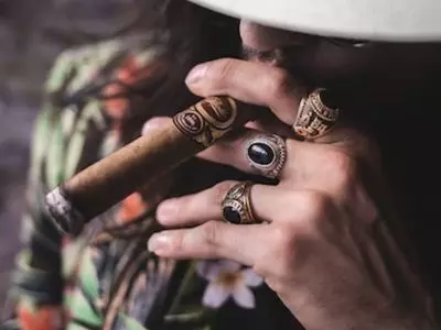 person smoking a large cigar with rings on their hand