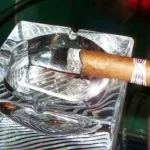 Cigar sitting on the side of a glass ashtray